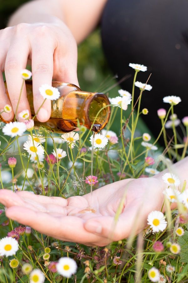 Versement d'huile de massage dans ma paume entourée de fleurs blanches et roses.